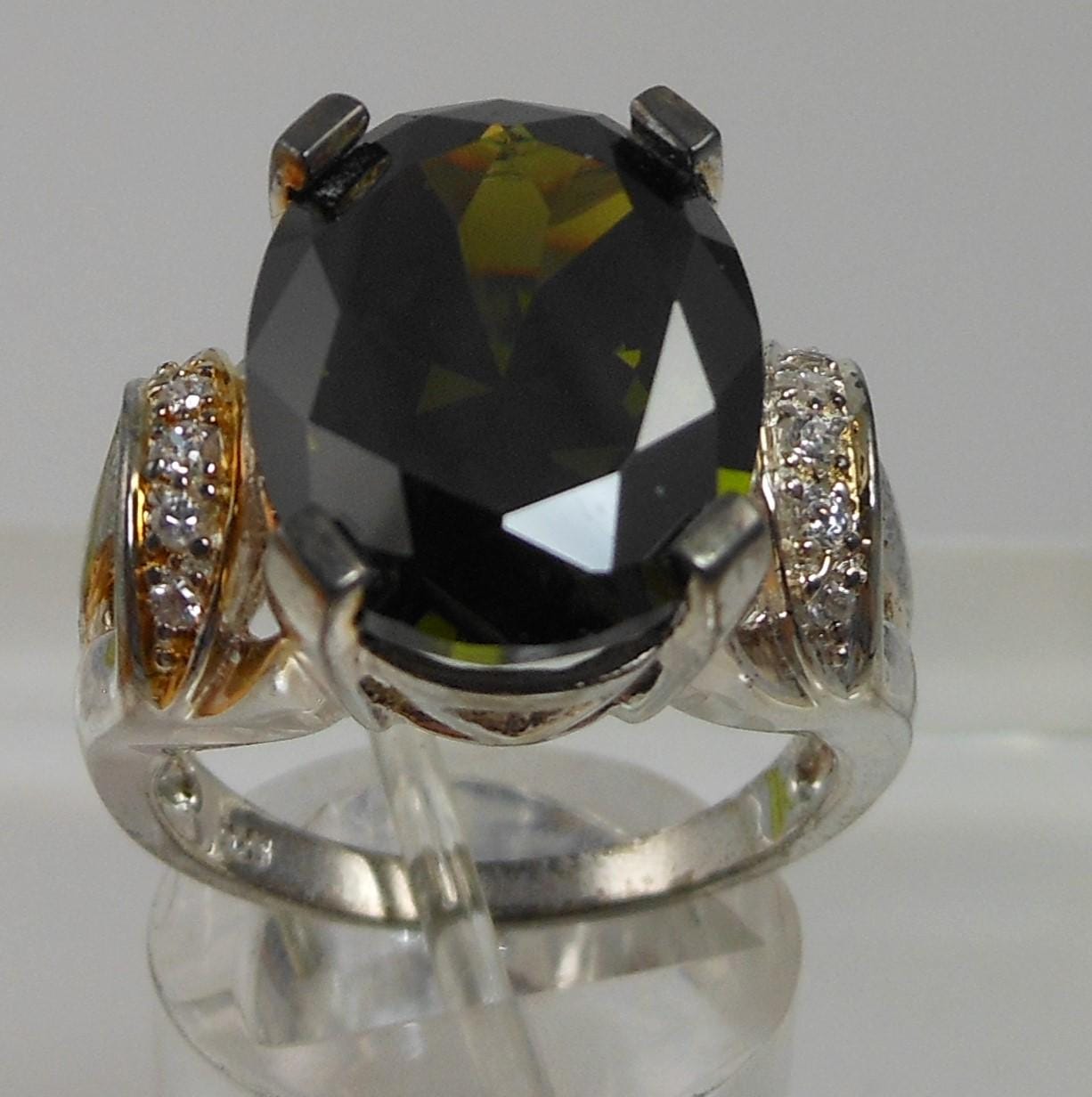 Ring with a large black gemstone and diamond-studded band on a reflective surface